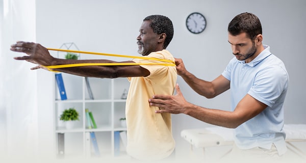 Elderly African American gentleman with a rehab therapist in the rehab gym working with yellow stretching bands