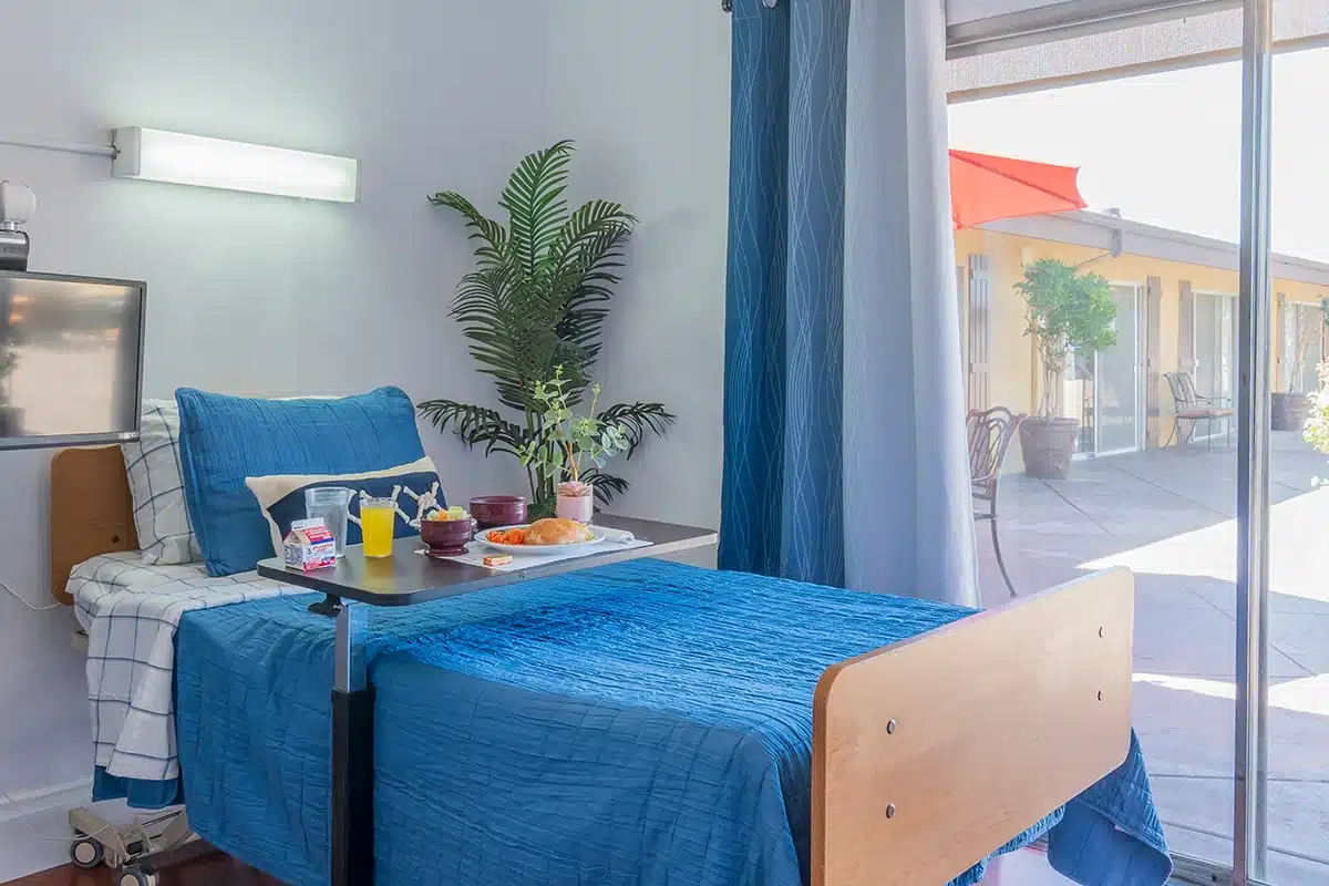 Close up of resident room with personal monitor, breakfast set up on bedside table and courtyard outside of slider