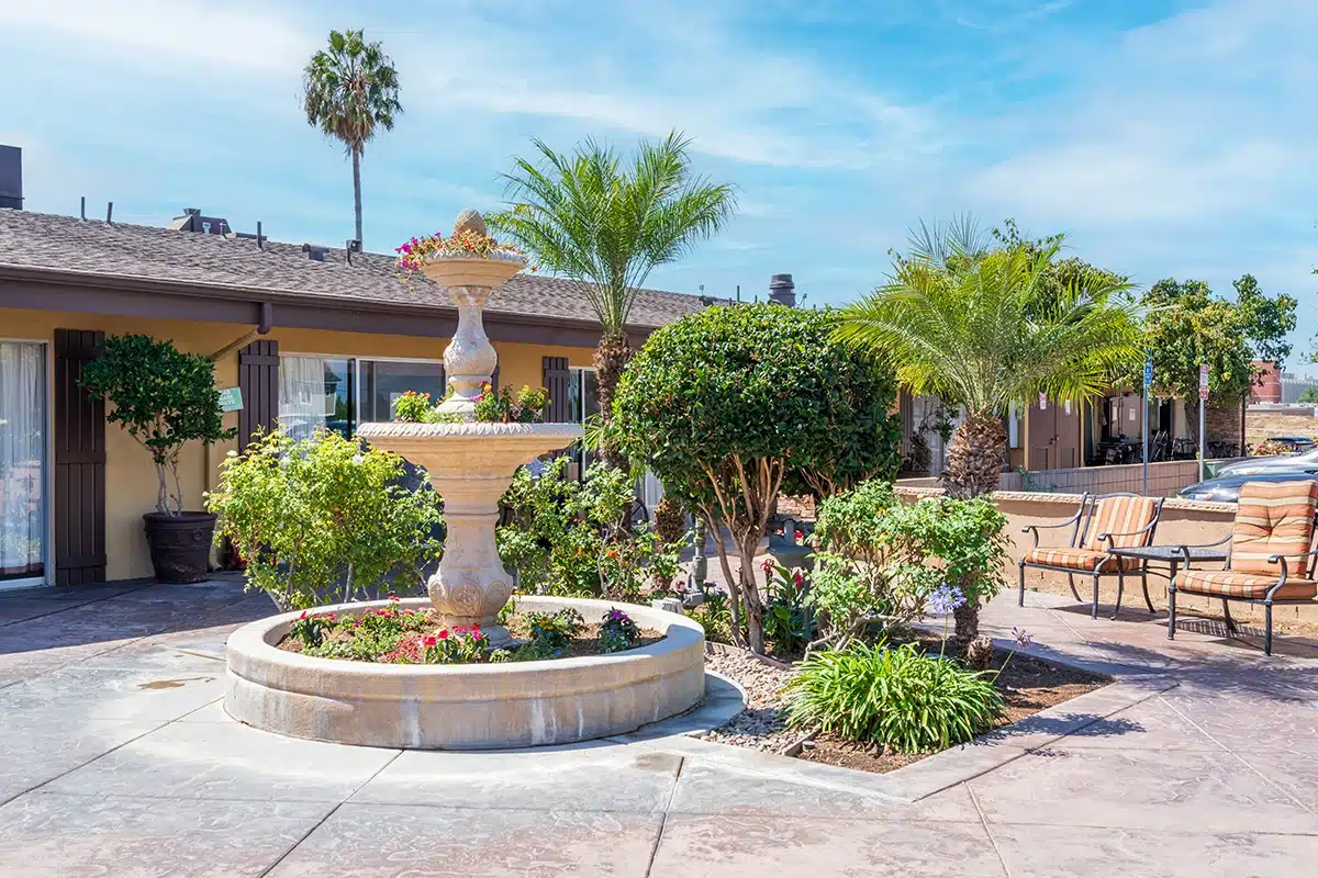 Outside courtyard with large fountain with flowers in it and orange cushioned chairs by palm trees